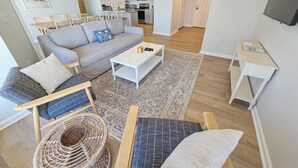 A modern living room with a grey sofa, a white coffee table, and a wicker chair. - 2106 Brighton | On Ocean | Top Floor | Resort Access (Myrtle Beach)