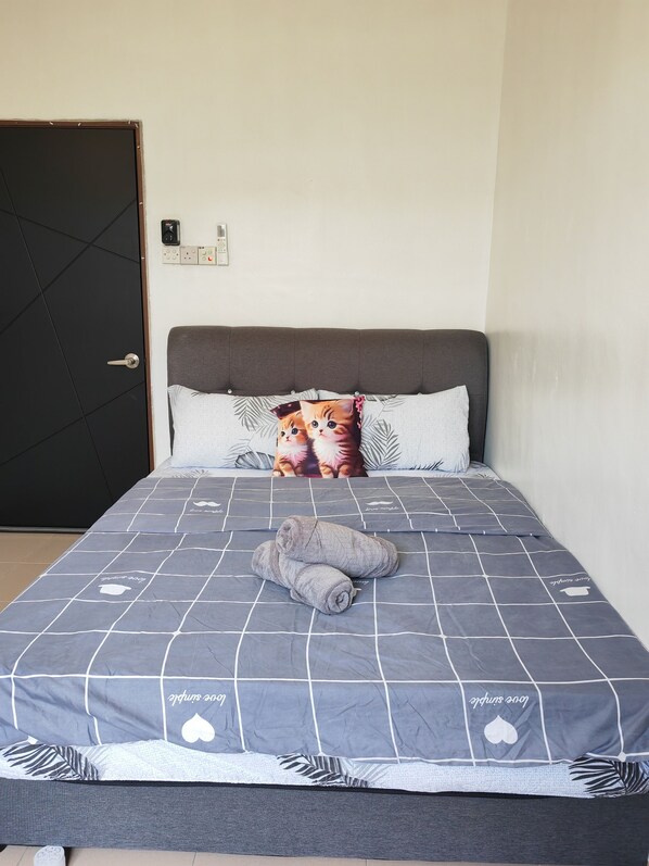 A neatly made bed with a grey quilt and a pillow with a cat design.