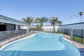 A swimming pool with a curved design, surrounded by a fence and palm trees. - 2 Mi to Golf: Poolside Paradise in Scottsdale! (Scottsdale)