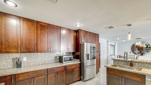 A kitchen with wooden cabinets, a stainless steel refrigerator, a microwave, and granite countertops. - 2 Mi to Golf: Poolside Paradise in Scottsdale! (Scottsdale)