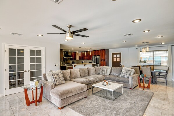 A spacious living room with a large sectional sofa, a glass coffee table, and a dining area with a chandelier. - 2 Mi to Golf: Poolside Paradise in Scottsdale! (Scottsdale)