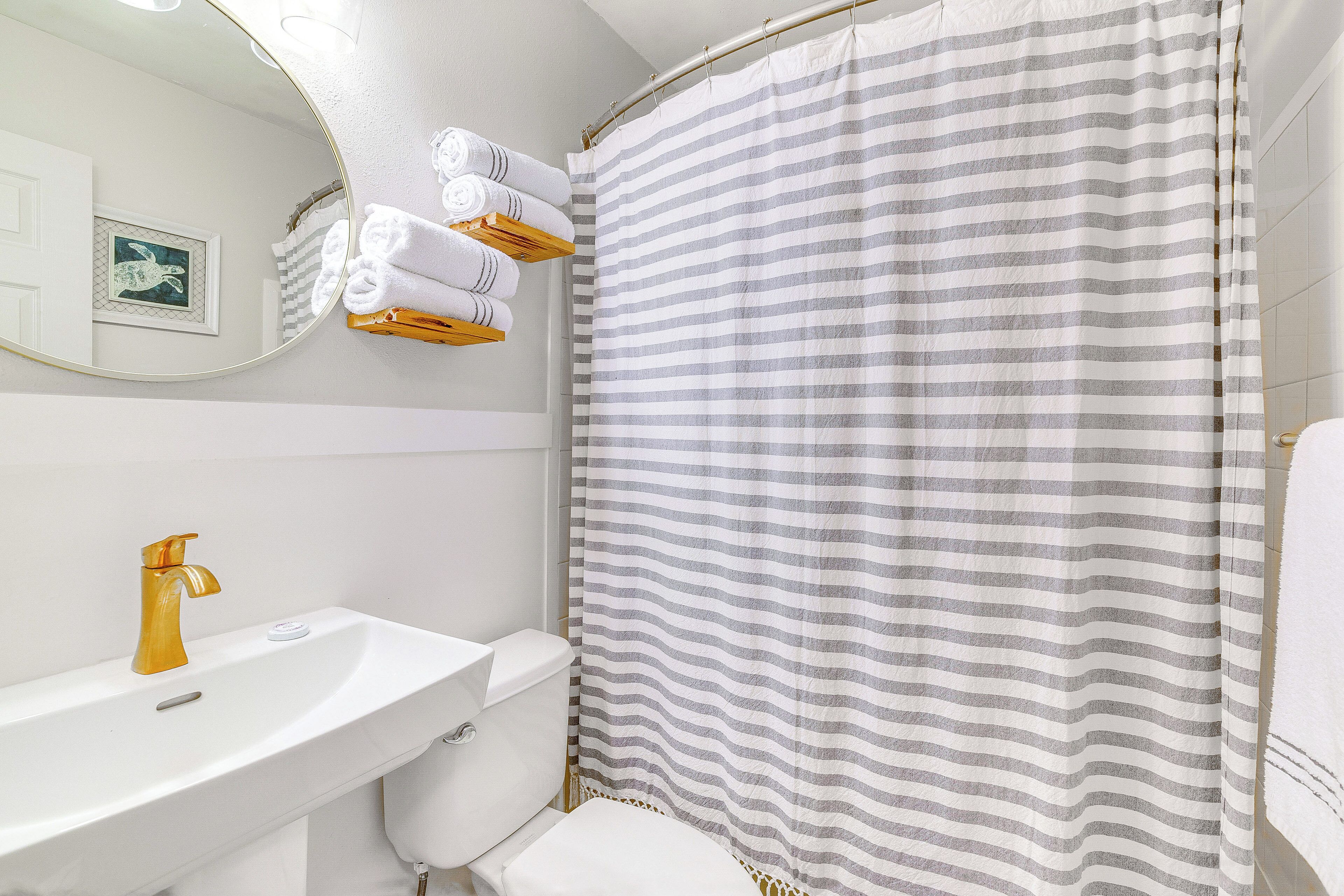 A bathroom with a white sink, gold faucet, and a striped shower curtain.