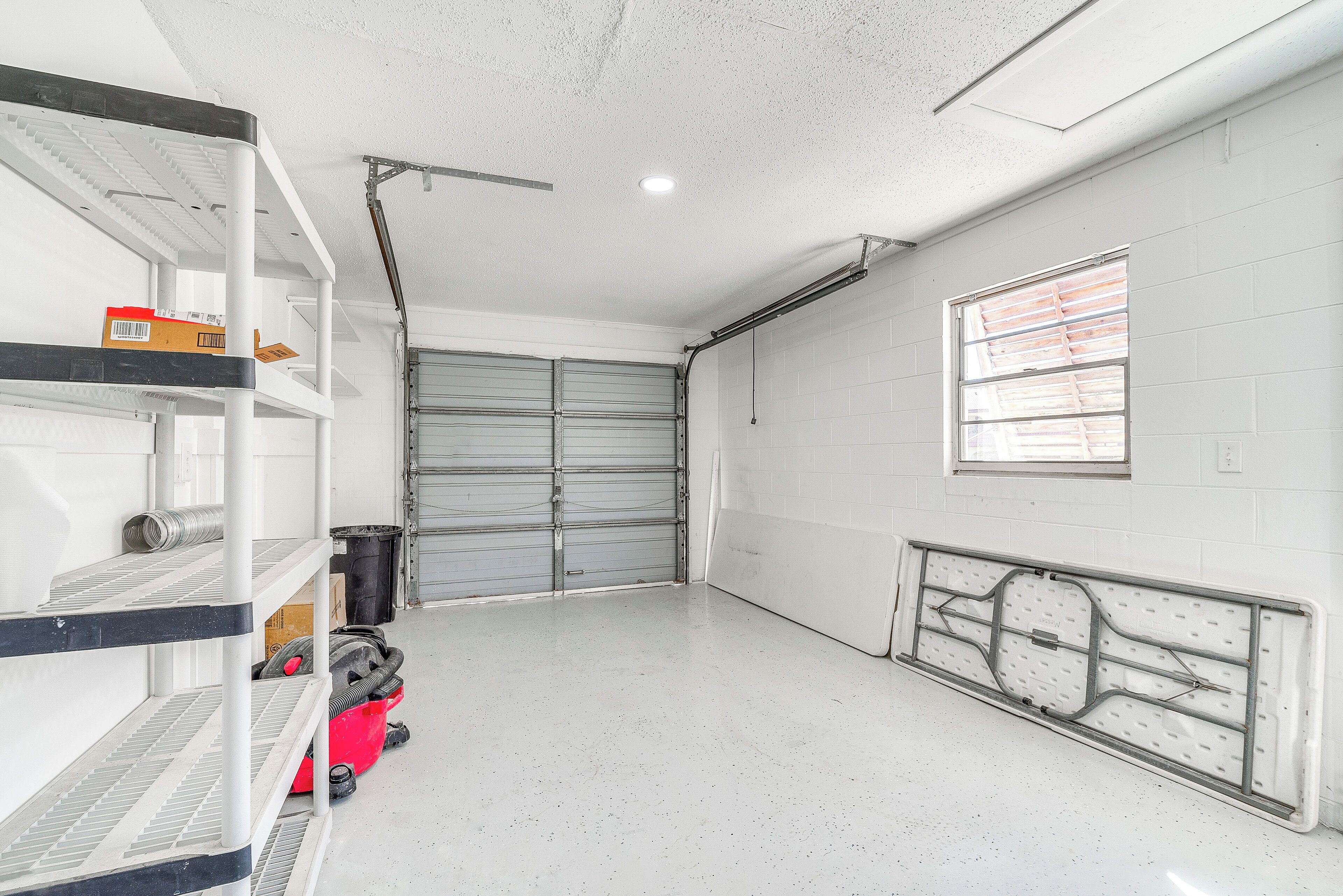 A garage with white walls, a concrete floor, and a window with blinds.