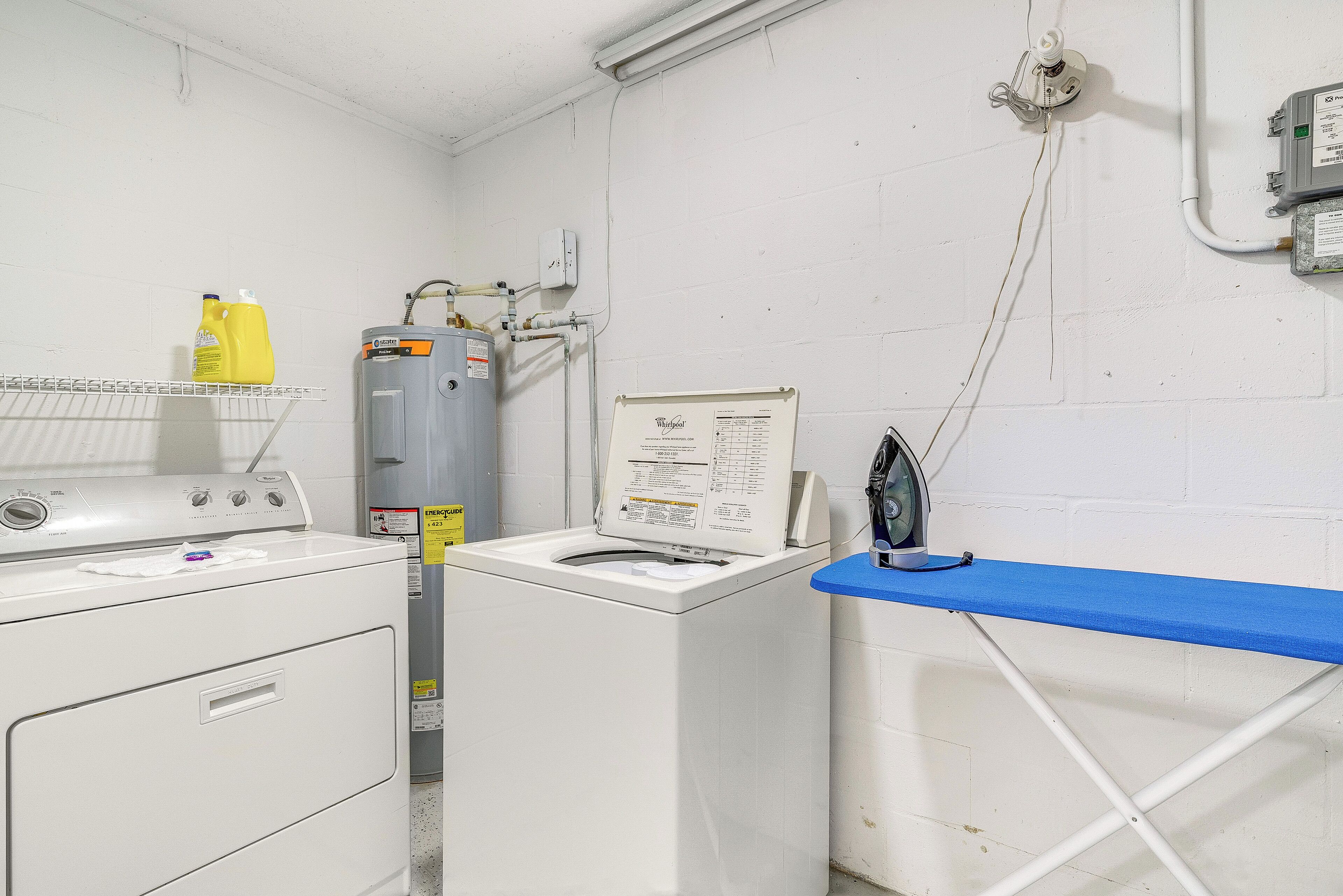 A laundry area with a washer and dryer, a water heater, and a blue ironing board.