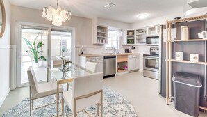 Une cuisine moderne avec une table à manger en verre, des chaises blanches, un lustre et des appareils électroménagers intégrés.