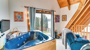 Ein modernes Badezimmer mit einer gläsernen Badewanne, einer Holzbalkendecke und einem großen Fenster mit Vorhängen.