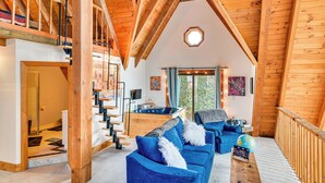 Ein großzügiger Loft-Raum mit hoher Decke, einer Holztreppe, einem gemütlichen blauen Sofa, einer Whirlwanne und einem großen Fenster mit Blick ins Freie.