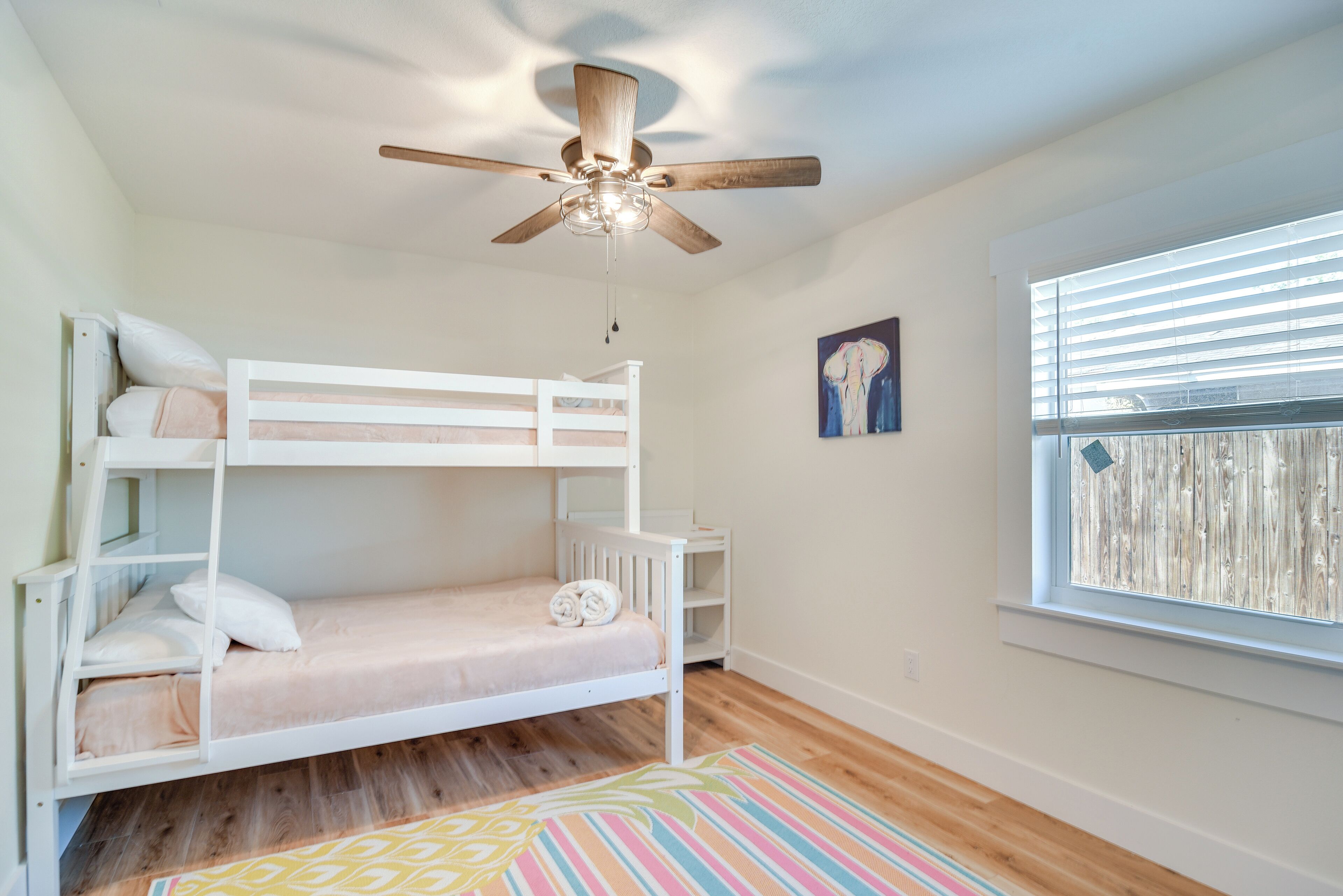 Quarto com beliche, ventilador de teto, janela com persianas e tapete colorido.