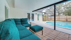 Ein überdachter Patio-Bereich mit Pool, einem smaragdgrünen Ecksofa und einem kleinen Tisch.