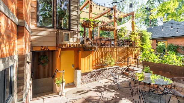 A patio area with a glass table and chairs, a wooden pergola with hanging plants, and a brick building with a 'hello' sign. - 2 Mi to Downtown Denver: Stylish Gem w/ Fireplace! (Denver)