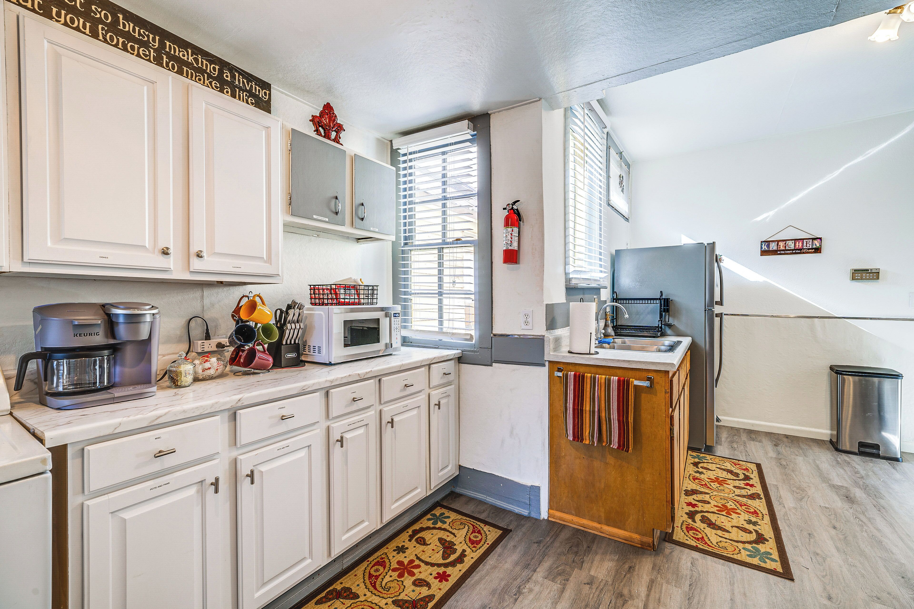 Una cocina compacta con armarios blancos, cafetera, microondas y refrigerador.