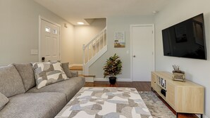 A living room with a grey sofa, a patterned rug, a wooden cabinet, a potted plant, and a TV on the wall.