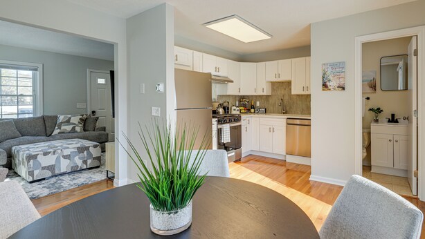 A modern kitchen with white cabinets, a central island, and a dining area with a round table and chairs.