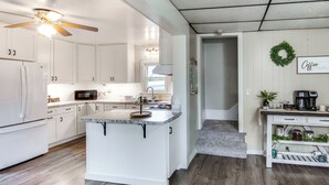 Une cuisine moderne avec des meubles blancs, un îlot central et un ventilateur de plafond.