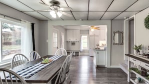 A spacious dining area with a wooden table and chairs, a ceiling fan, and a view of the kitchen and living areas. - Family-friendly Altoona Abode w/ Spacious Patio! (Altoona)