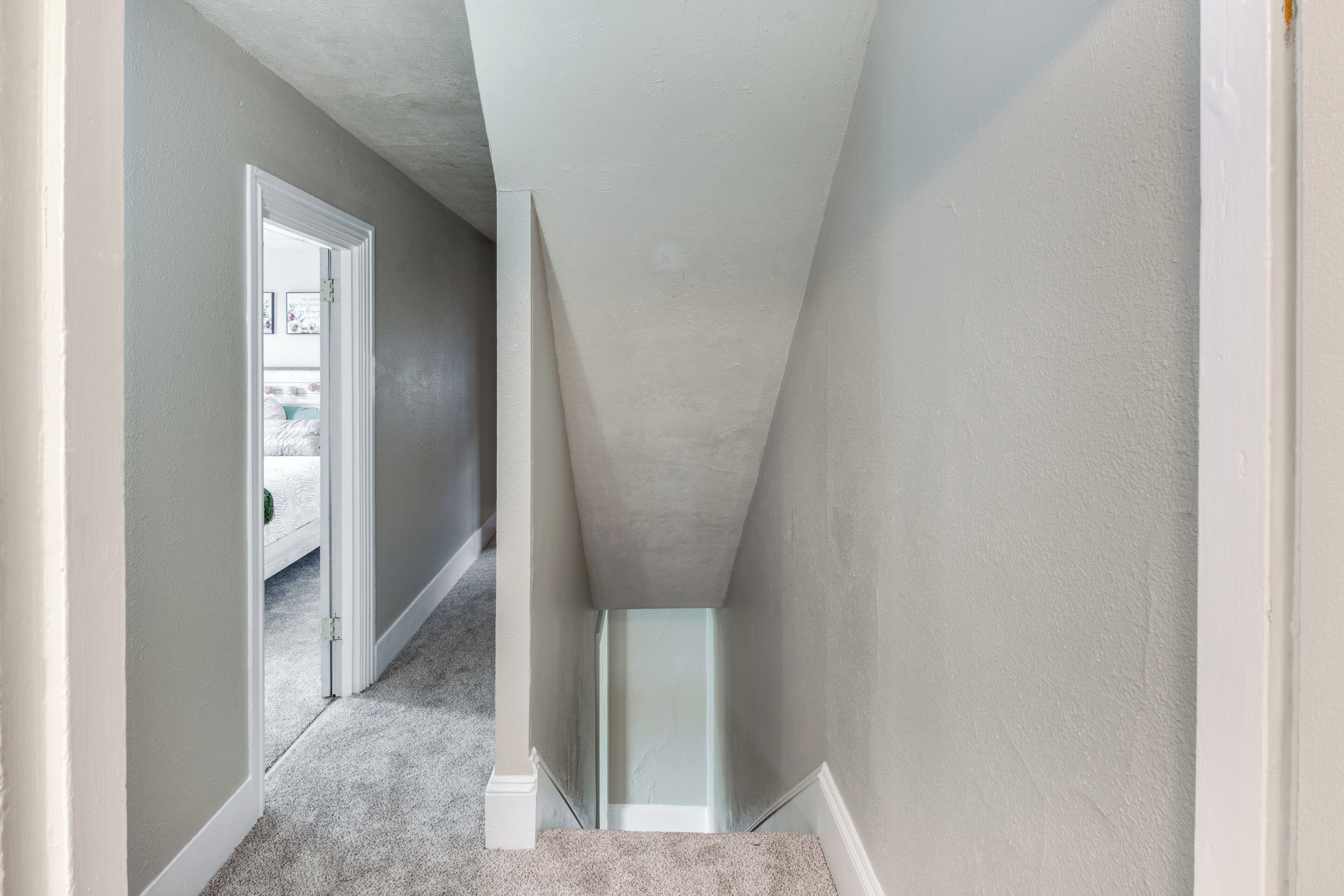 Un couloir étroit, doté d’un sol recouvert de moquette et d’une porte donnant sur une chambre à coucher.
