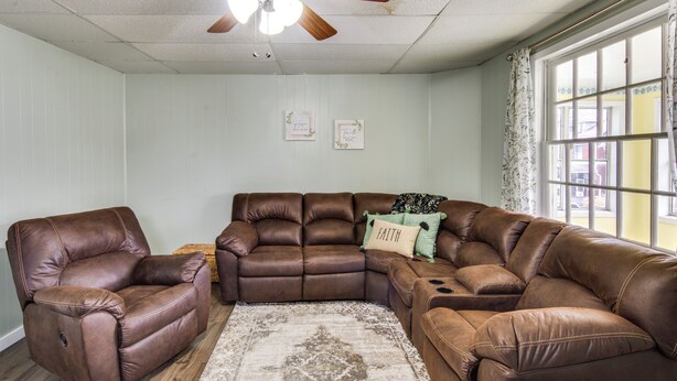 Un salon avec un canapé d’angle en cuir marron, un fauteuil inclinable et un ventilateur de plafond.