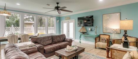 A spacious living room with a brown leather sofa, a wooden coffee table, and a television mounted on the wall.