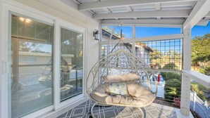 A covered porch with a hanging chair, large windows, and a view of the neighborhood. - St Simons Island Townhome w/ Balcony + Ocean View! (St. Simons Island)