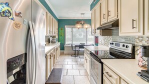 A kitchen with a stainless steel refrigerator, a built-in oven, and a microwave. There is a window with blinds, a chandelier, and a tiled backsplash. - St Simons Island Townhome w/ Balcony + Ocean View! (St. Simons Island)