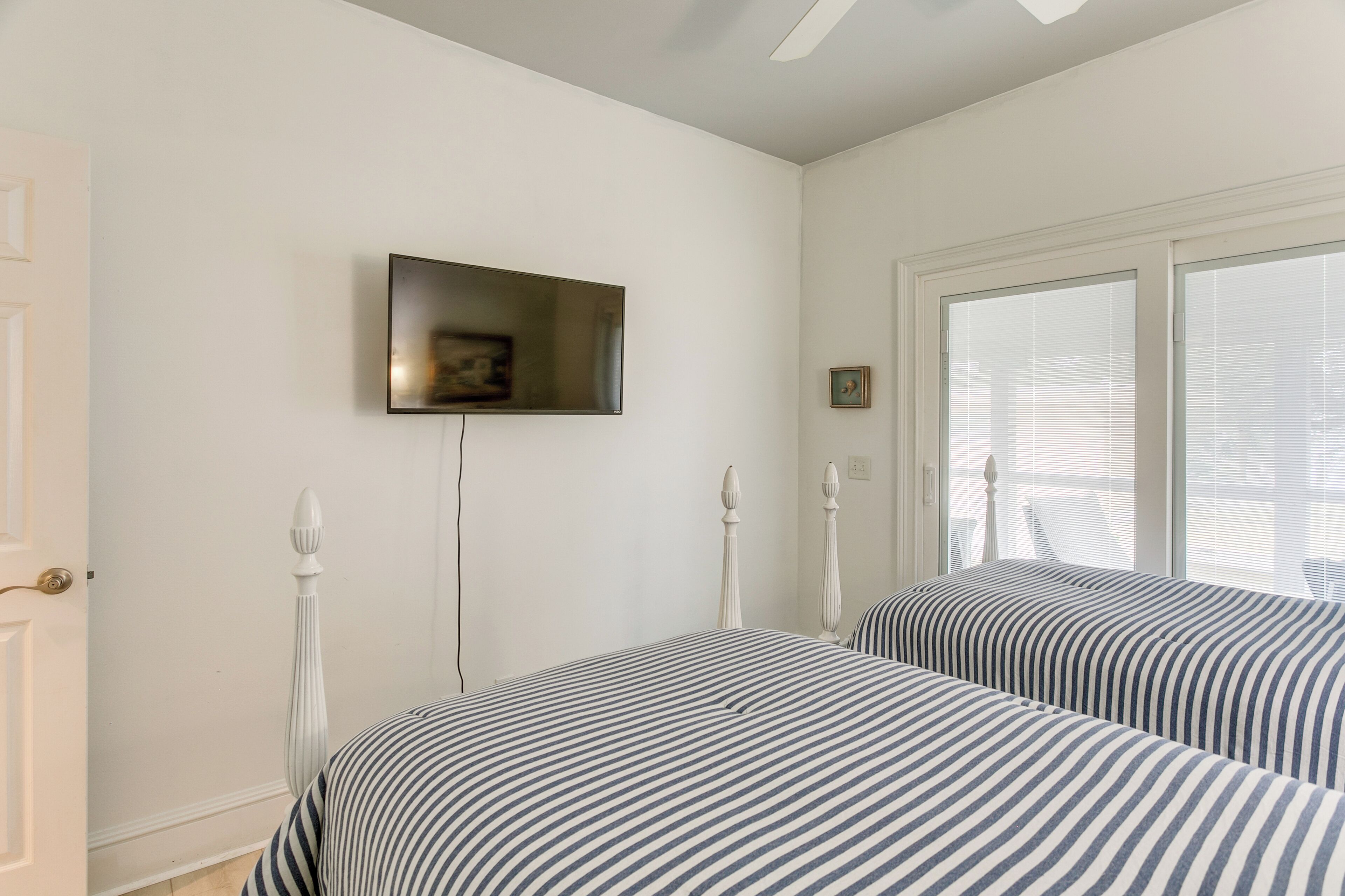 A bedroom with two beds, a TV mounted on the wall, and a window with blinds.