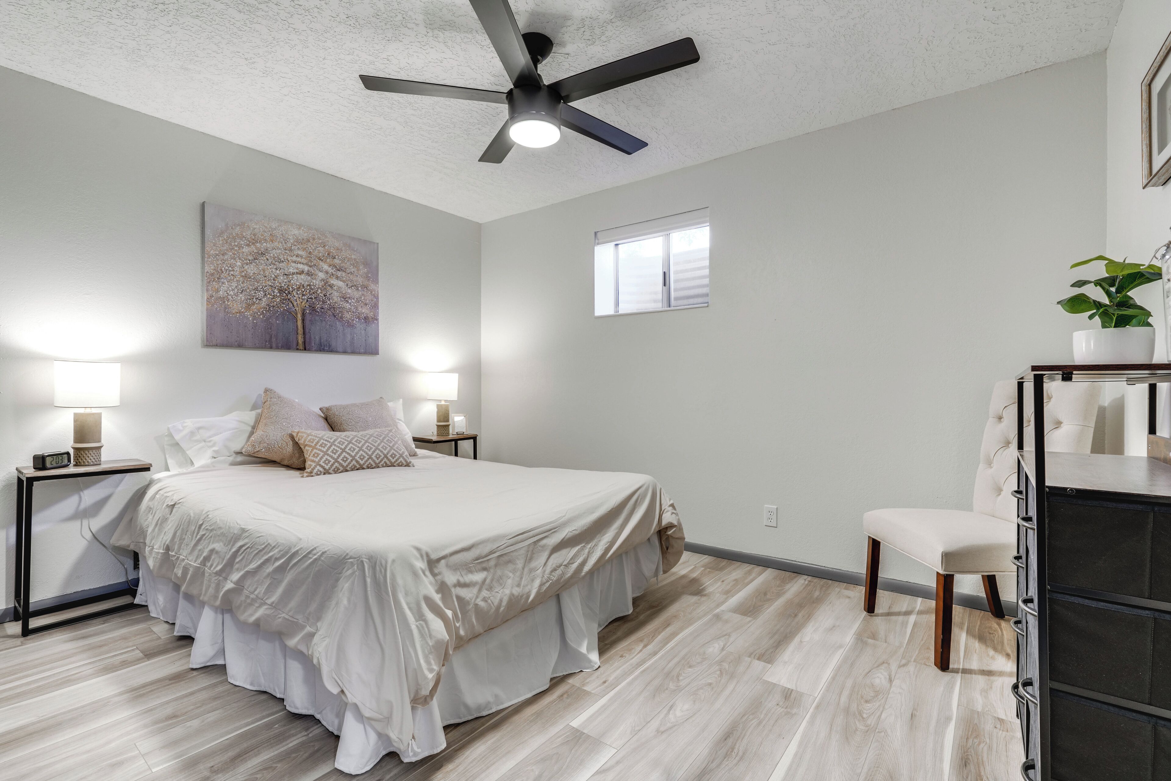 Un dormitorio con cama, mesitas de noche, ventilador de techo, ventana y cómoda.
