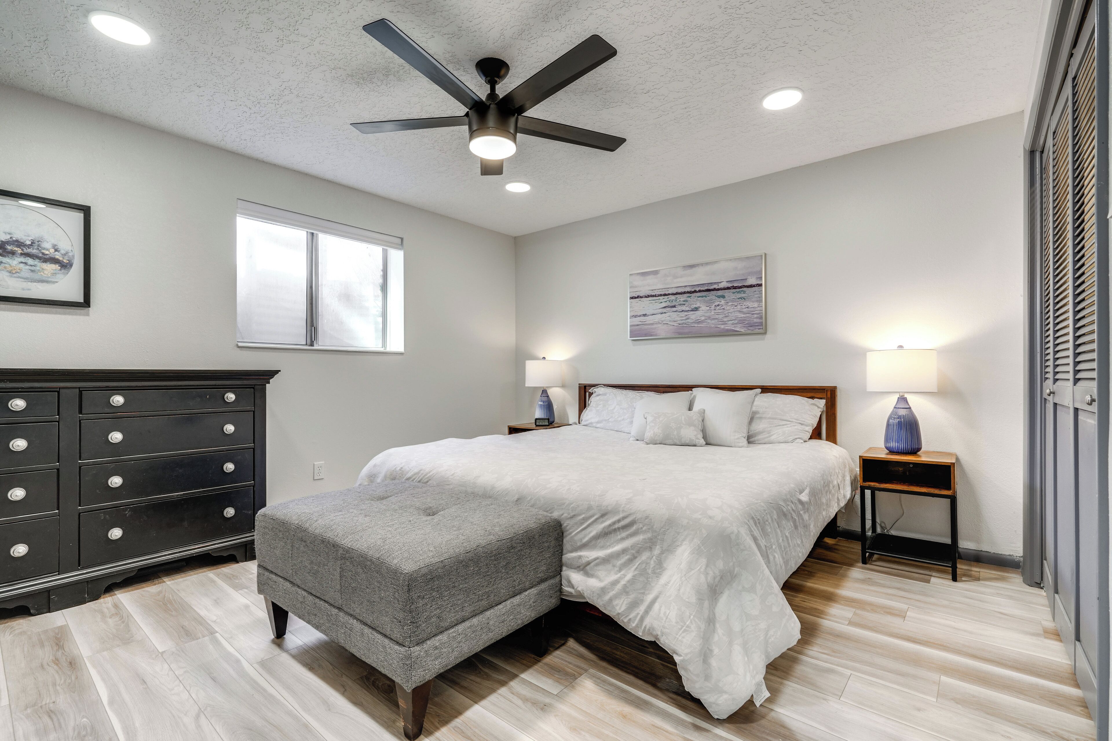 A bedroom with a bed, a dresser, a nightstand, a ceiling fan, and a window.