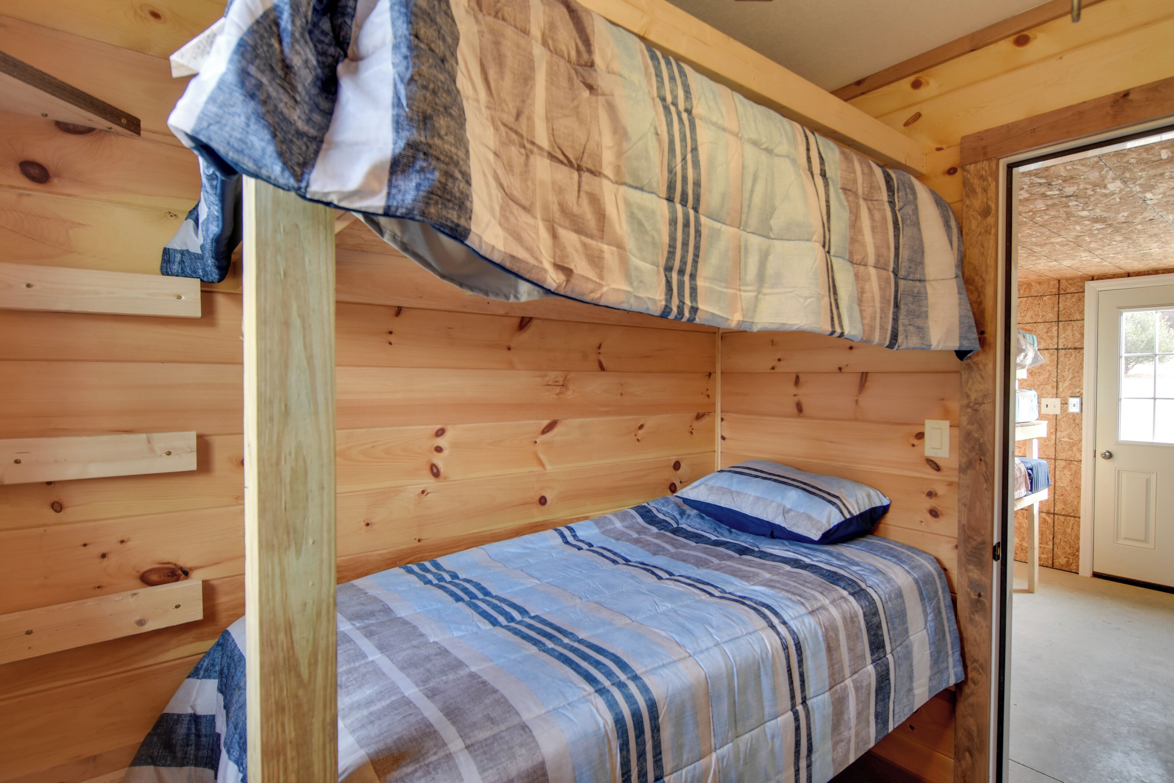 Une chambre de chalet en bois avec un lit superposé et un lit simple, agrémentée d’une couverture à carreaux et d’une tête de lit en bois.