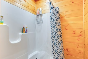 Un baño de cabaña de madera con ducha, una bañera blanca y un estante con artículos de aseo.