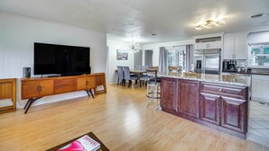 A spacious kitchen with a central island, a dining area with chairs, and a large flat-screen TV mounted on a wooden cabinet.