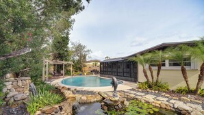 A backyard with a swimming pool, a small waterfall, and a pond with lily pads.