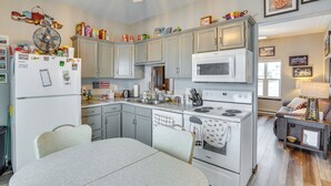 Una cocina con una mesa de comedor, electrodomésticos blancos y diversos objetos sobre las encimeras.