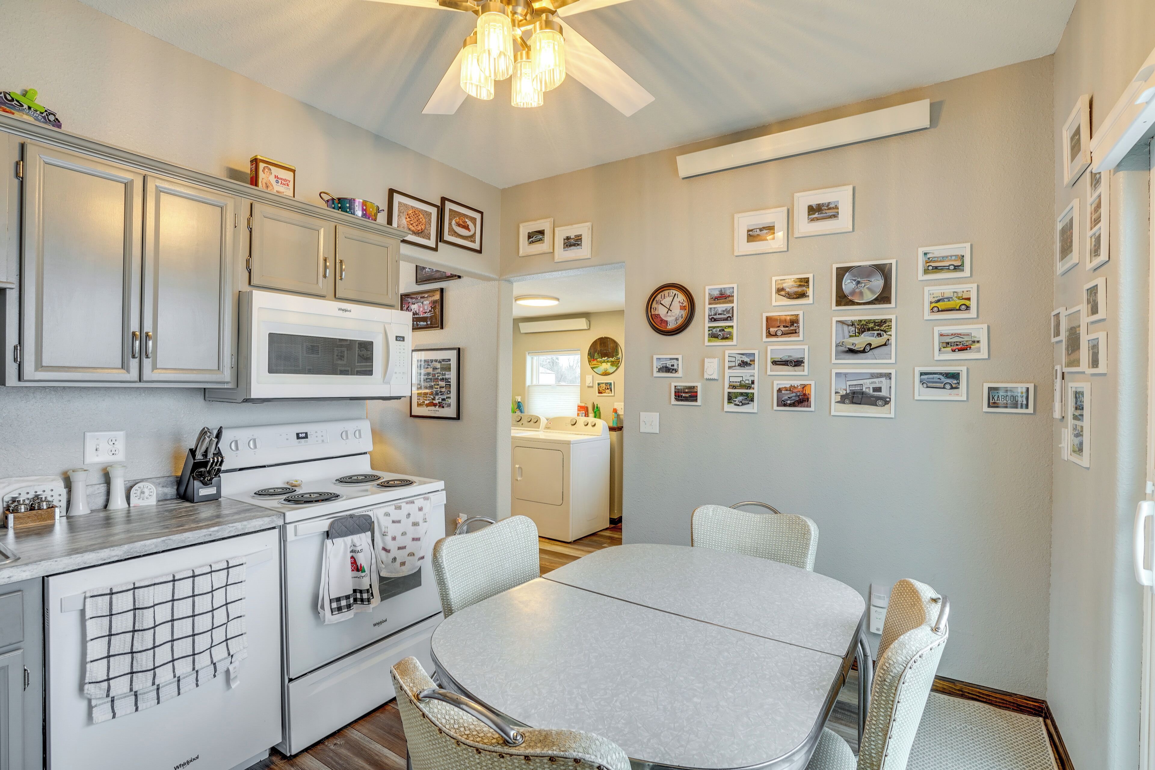 A kitchen with white appliances, a dining table, and chairs. There are framed pictures on the walls.