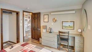 Un dormitorio con cama, cómoda, silla, escritorio y espejo. Hay una puerta que da a otra habitación.
