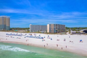 Een strandresort met meerdere hotelgebouwen, een zandstrand en parasols.