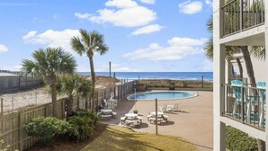 A pool area with lounge chairs and palm trees, overlooking a beach and ocean. - Moondrifter 207 - Condo with Spectacular Views (Panama City Beach)