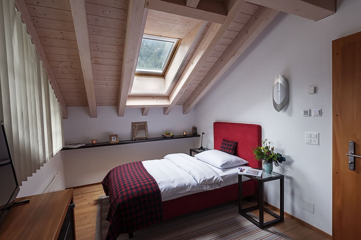 A bedroom with a skylight, a red headboard, a bedside table with a plant, and a red and black checkered blanket.