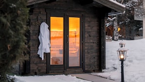 A wooden cabin with a glass door, a white robe hanging on the door, and a snow-covered landscape with mountains in the background. - Mirabeau Alpine (Zermatt)