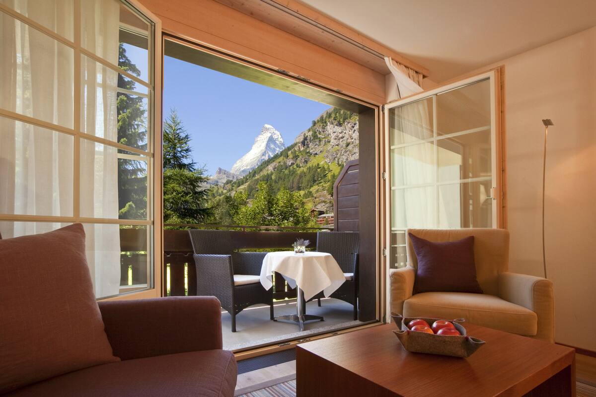 A room with a sliding glass door leading to an outdoor seating area with a table and chairs, a sofa, and a small table with fruit.