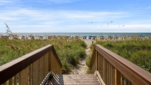 Une promenade en bois menant à une plage où l’on trouve des parasols et des chaises de plage.