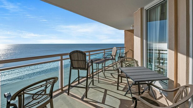 A balcony with a view of the ocean, furnished with chairs and a table.