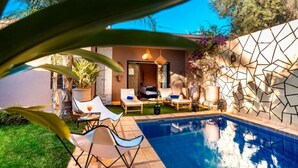 A pool area with lounge chairs and a small table, surrounded by a geometric wall and greenery. - Villa Cosy Piscine 5 Km du Centre Ville 4 Suites (Marrakech)
