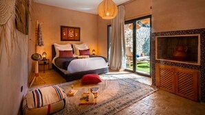 A bedroom with a large bed, a fireplace, a view of a garden, and a cozy atmosphere. - Villa Cosy Piscine 5 Km du Centre Ville 4 Suites (Marrakech)