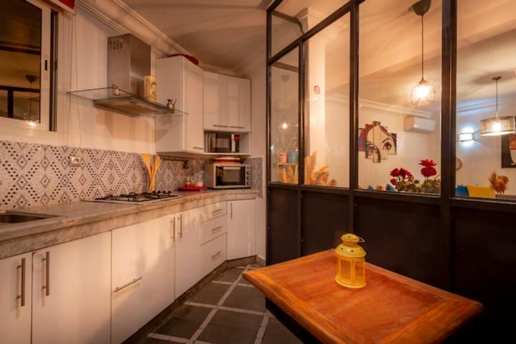 Una cocina con armarios blancos, un microondas y una estufa. Hay una mesa de madera con un farol amarillo encima.