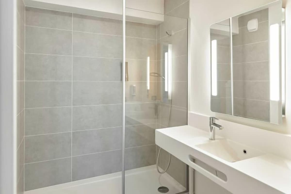 Un baño moderno con cabina de ducha acristalada, un lavamanos blanco y un espejo grande.
