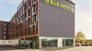 A modern B&B hotel with a prominent sign, large windows, and a parking lot. - B&B Hotel Marne-La-Vallée Val D'Europe (Serris)