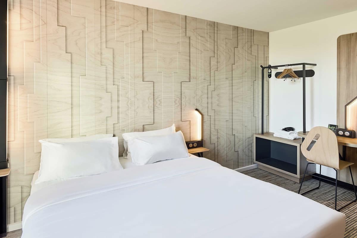 Ein Hotelzimmer mit einem Bett, einem Schreibtisch, einem Stuhl, einem Kleiderschrank und einem Spiegel.