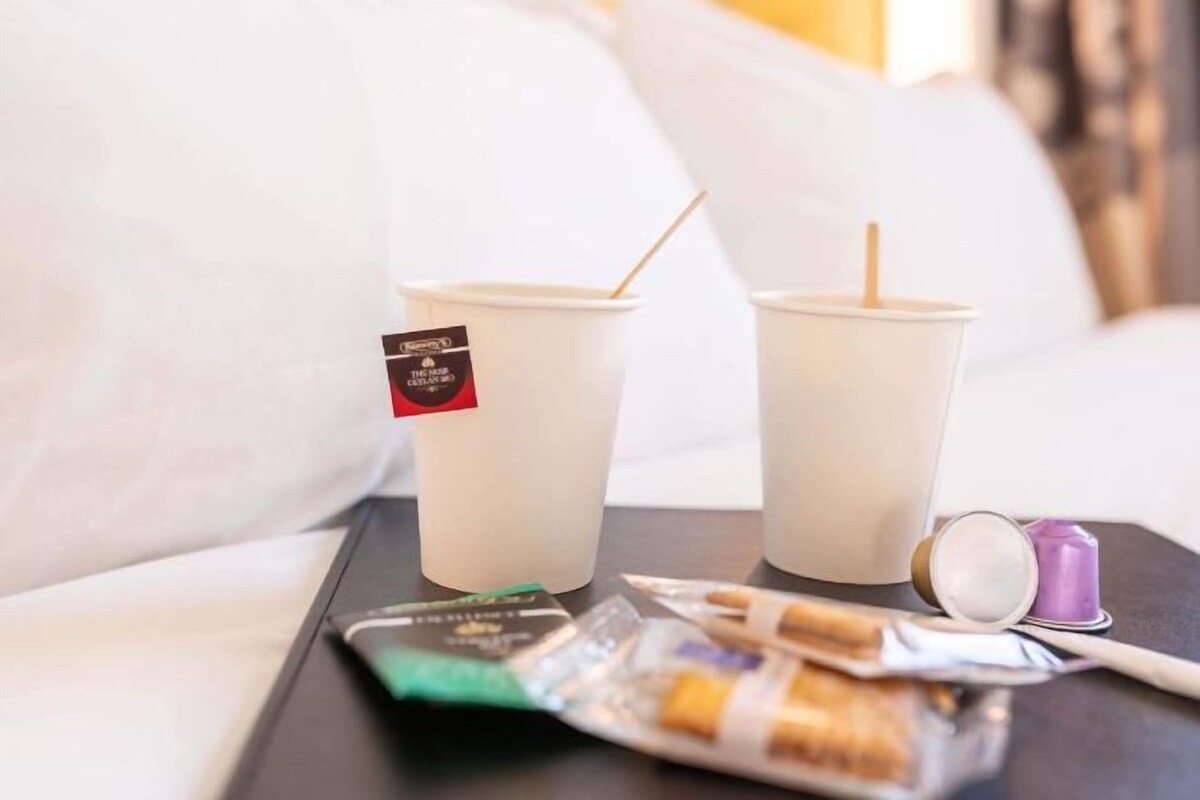 Un plateau avec deux gobelets jetables, un paquet de collations et un petit récipient, le tout posé sur un lit.