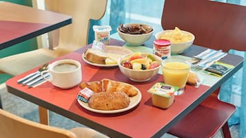 A breakfast table with croissants, fruit, yogurt, coffee, and juice.