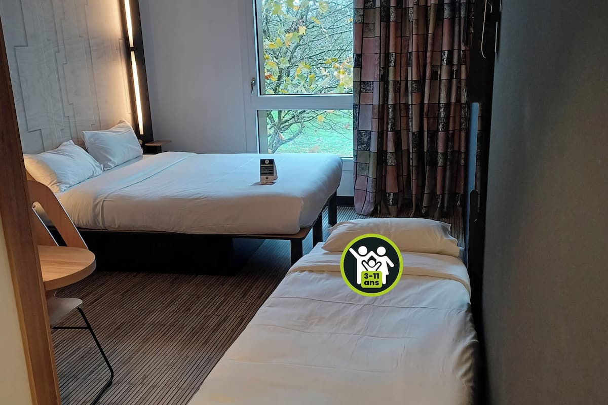 Ein Hotelzimmer mit zwei Betten, einem kleinen Tisch und einem Fenster mit Vorhängen.